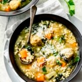 the wedding soup in a black bowl with a silver spoon in it from overhead