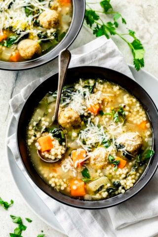 the wedding soup in a black bowl with a silver spoon in it from overhead