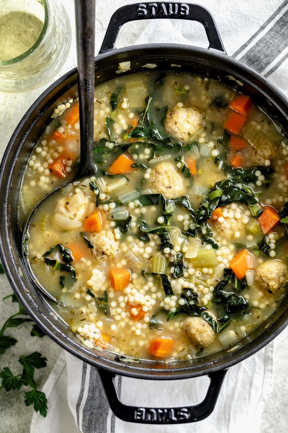 the wedding soup in a black Dutch oven with two handles from overhead with a black ladle in it