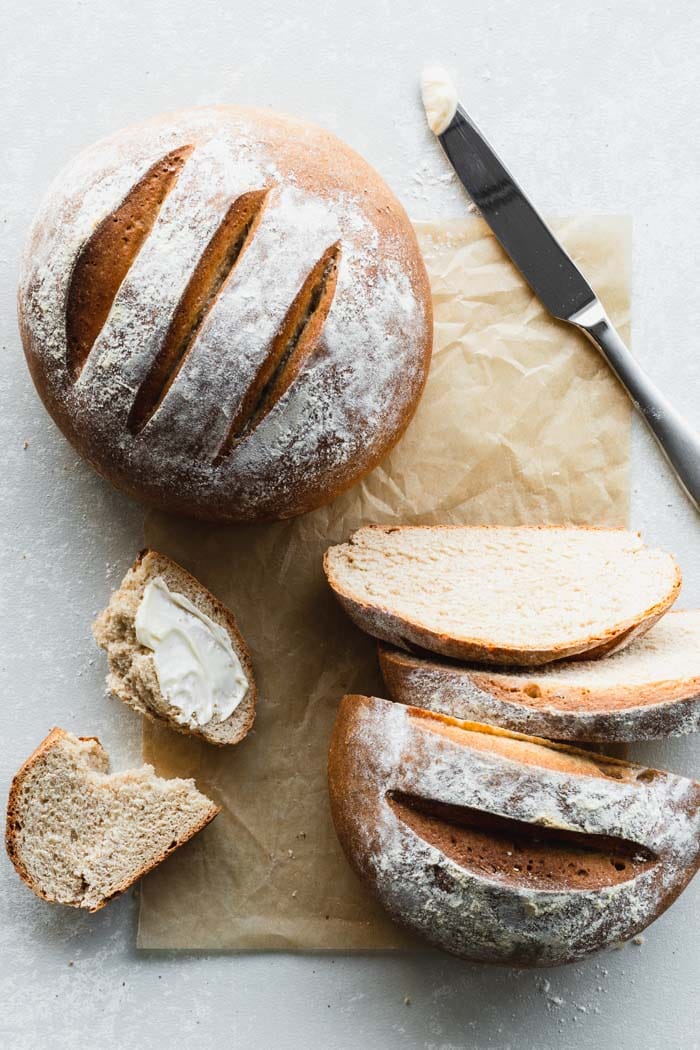 Whole loaf and cut loaf of bread on parchment paper next to knife