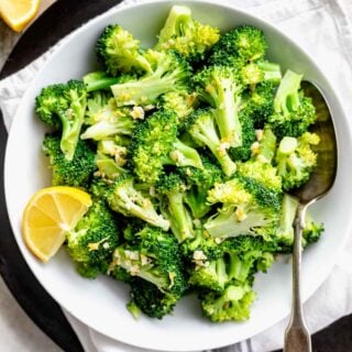 overhead white bowl with broccoli, lemon wedges and spoon