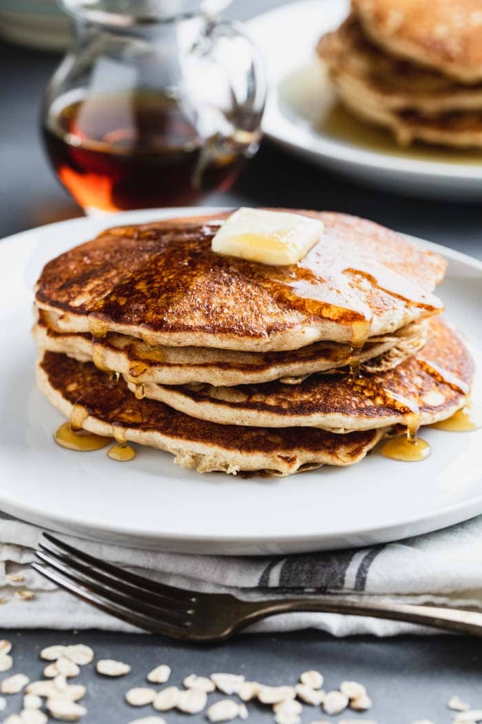 a tall stack of pancakes with butter on top and maple syrup poured over them