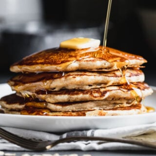 a stack of pancakes from the side with syrup drizzling over them