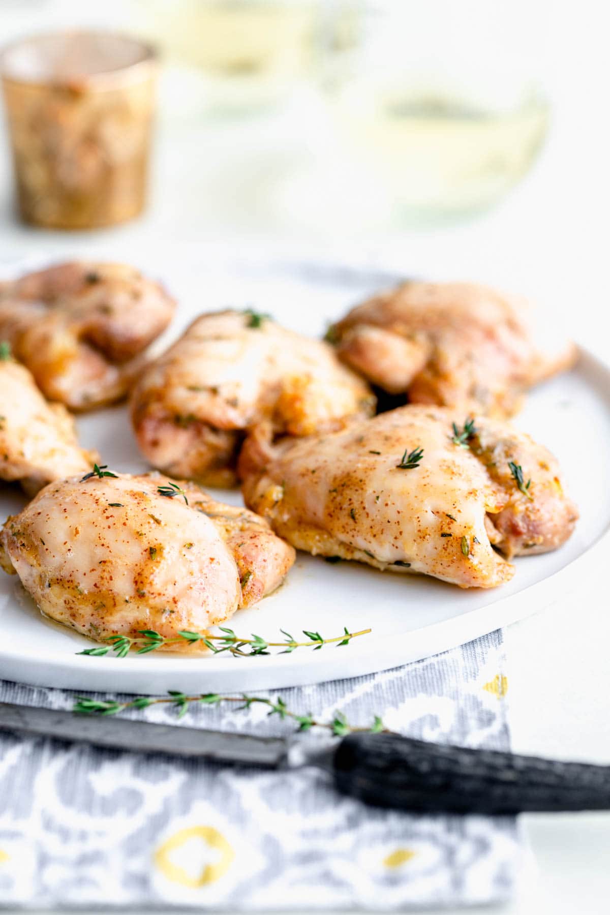 Chicken thighs on a plate from the side with a black faux bone handled knife in the foreground
