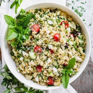 a white bowl with mixed together quinoa salad in it with mint garnish