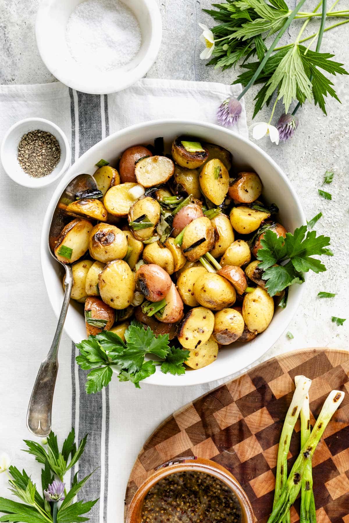 grilled potatoes in a white bowl with a small wooden cutting board with the grilled green onions on it
