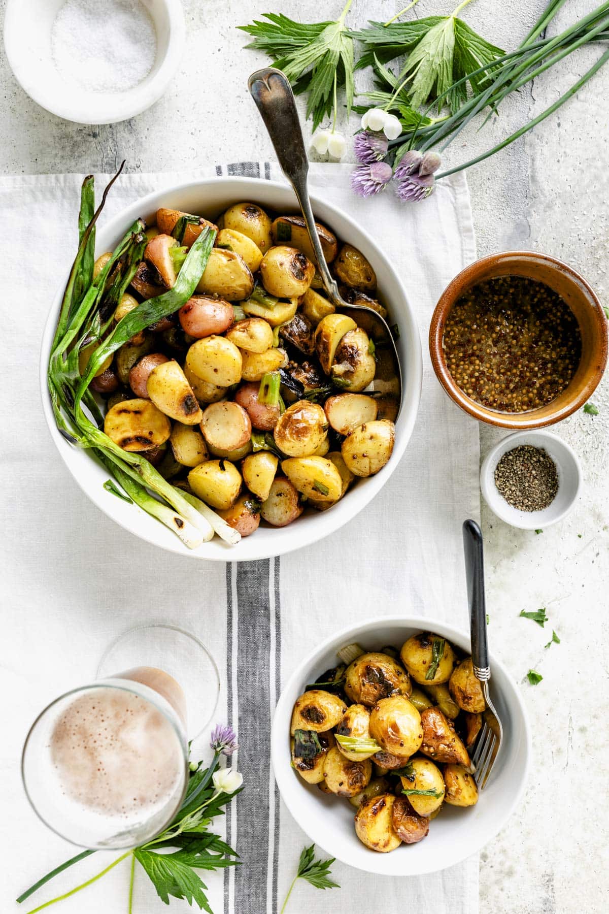 overhead of two bowls with grilled potatoes and a ceramic crock with whole grain mustard in it
