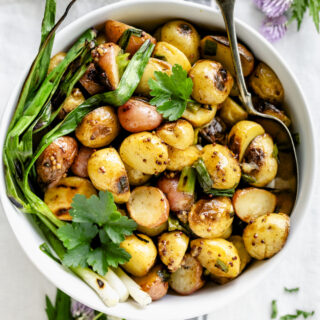 a white bowl with grilled potatoes in it with a couple of grilled scallions on the side