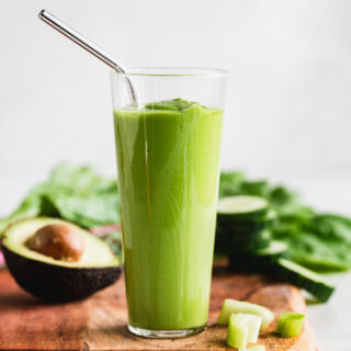 Green smoothie on a wood cutting board surrounded by ingredients