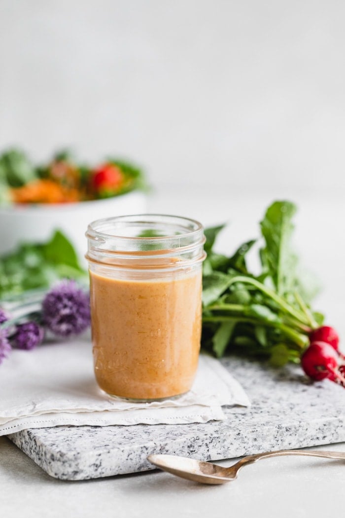 a jar of peanut dressing with lots of veggies and radishes