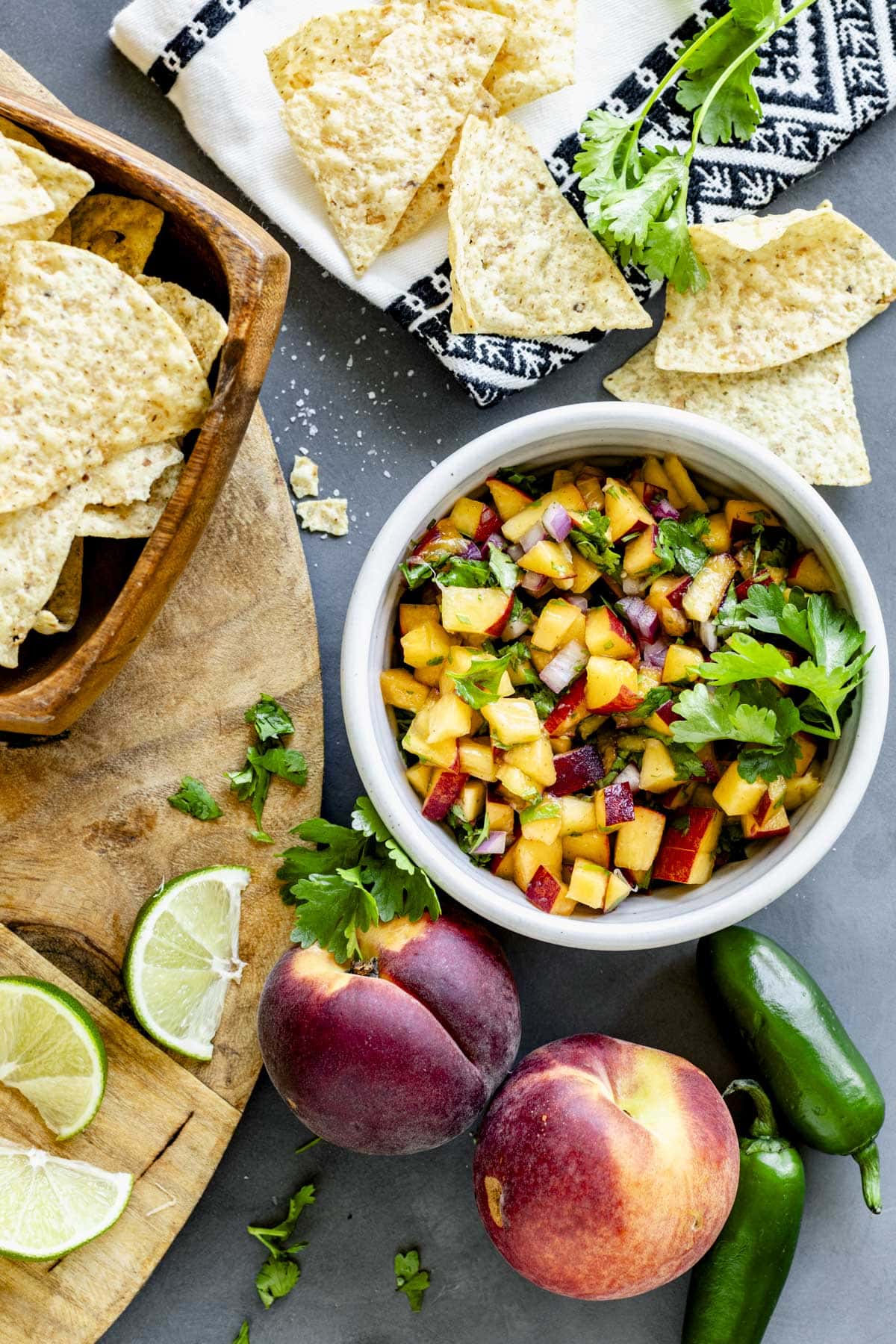 a bowl of peach salsa with whole fresh peaches, jalapenos and lime wedges