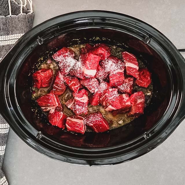 Beef and salt added to mixture in slow cooker.