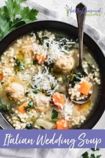 Italian wedding soup in a black bowl with a spoon up close