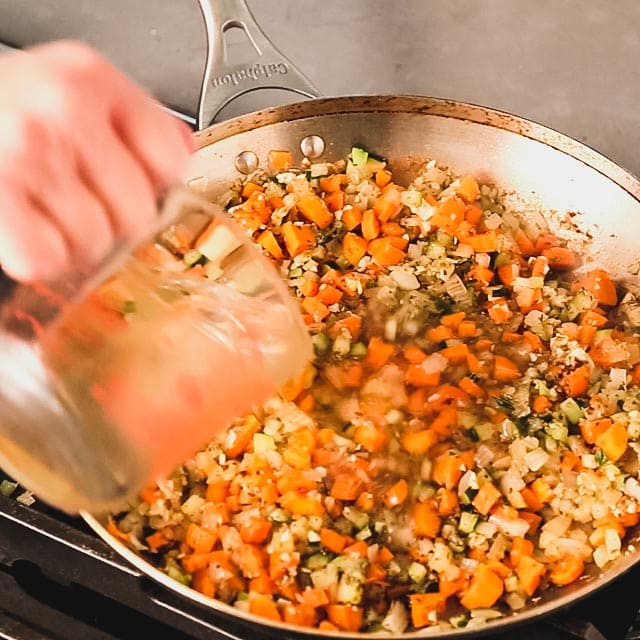 Adding wine to a large skillet with vegetables