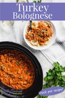 Overhead shot of white bowl of slow cooker bolognese with pasta next to slow cooker filled with bolognese and and fresh herbs