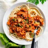 a white pasta bowl with a serving of pasta with bolognese sauce spooned over it