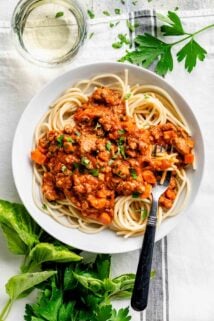 a white pasta bowl with a serving of pasta with bolognese sauce spooned over it