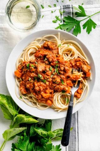 a white pasta bowl with a serving of pasta with bolognese sauce spooned over it