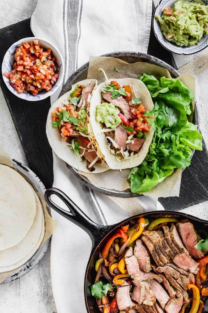 Steak fajitas with a skillet of peppers and steak, a plated serving and some condiments