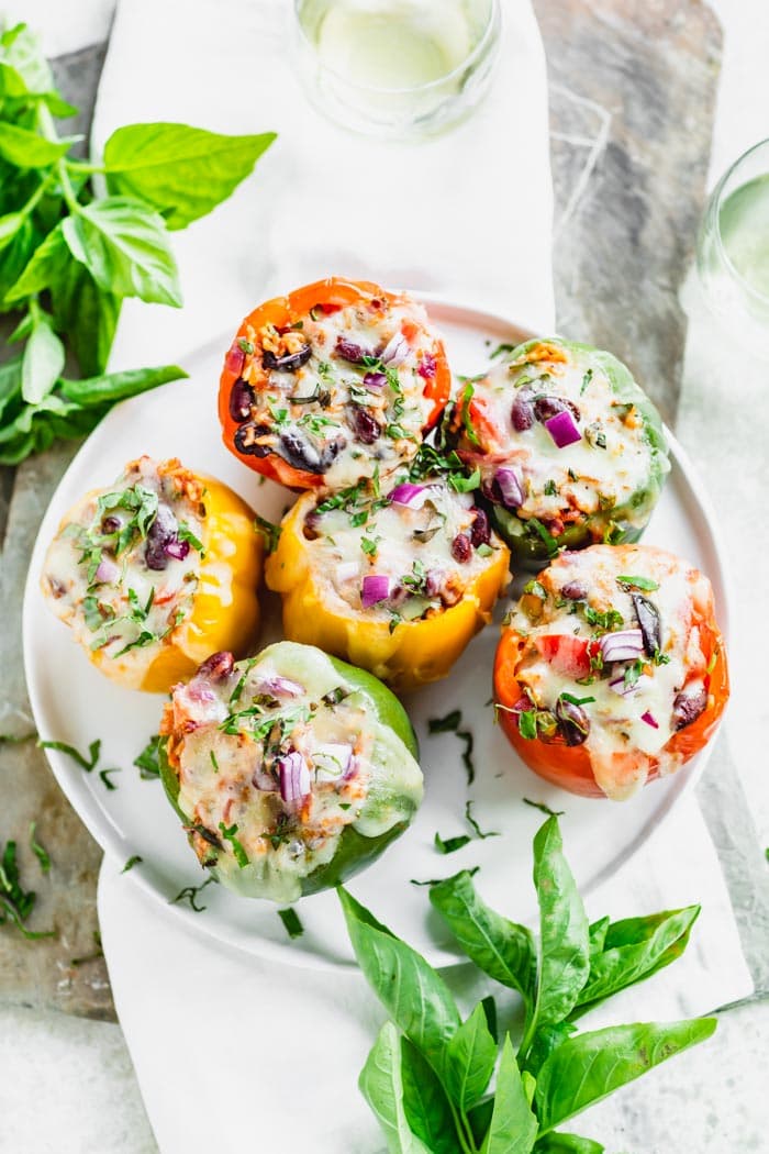 overhead of a platter of stuffed peppers with melted cheese and basil sprigs