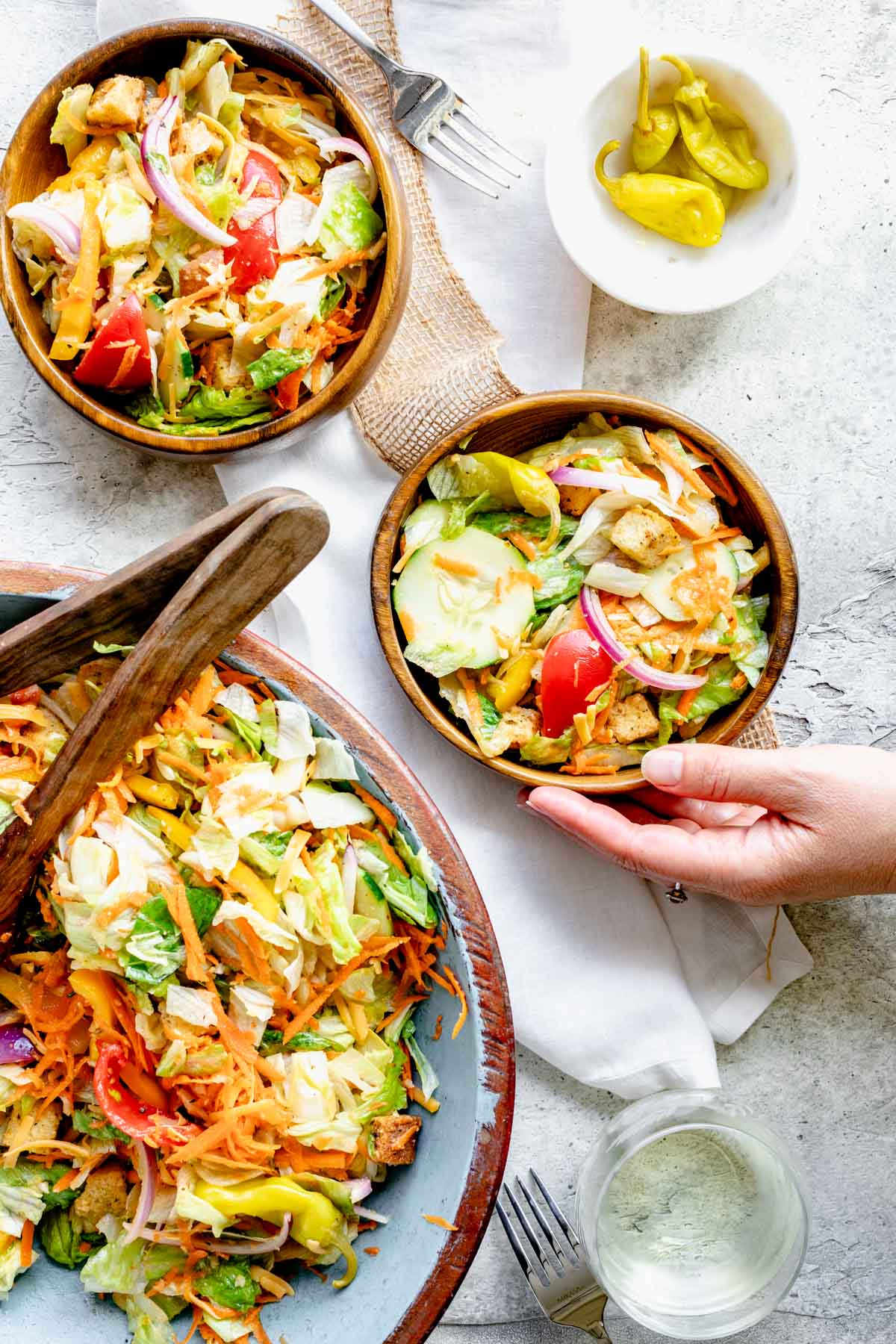 two bowls of salad and the salad bowl. a hand taking one of the bowls out.