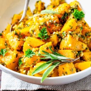 garlic herb steamed butternut squash in a white bowl with chopped herbs and sage sprig