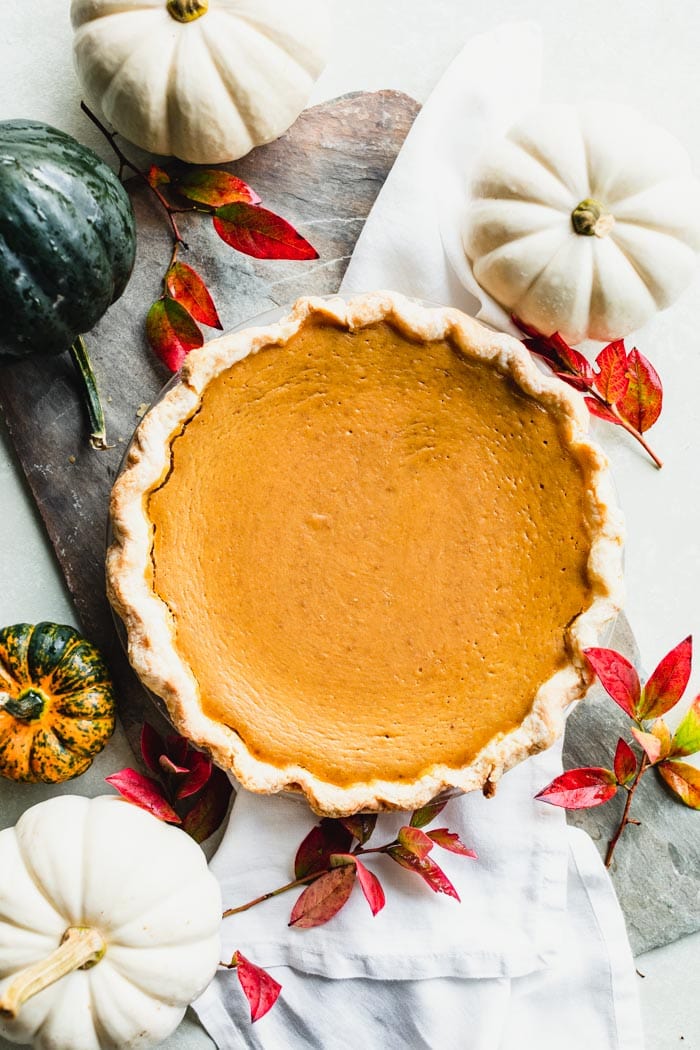 overhead of an uncut pumpkin pie with white pumpkins and fall leaves