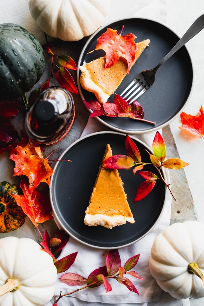 two plates of pie with gourds, a bottle of bourbon and fall leaves
