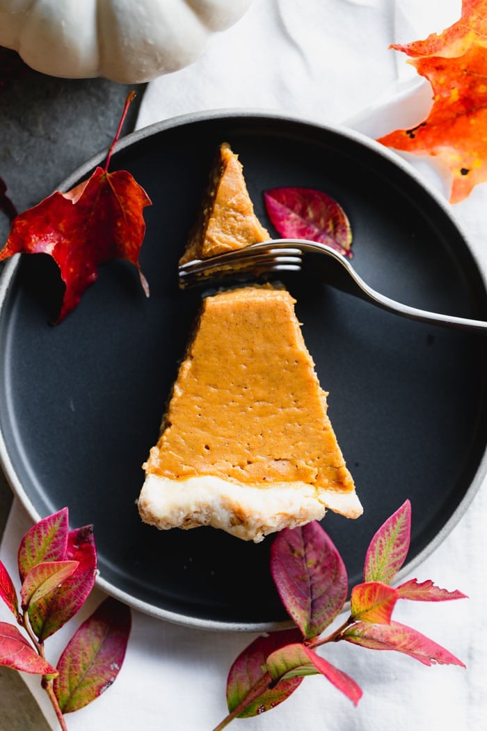 A slice of pie on a black plate with a fork cutting into it