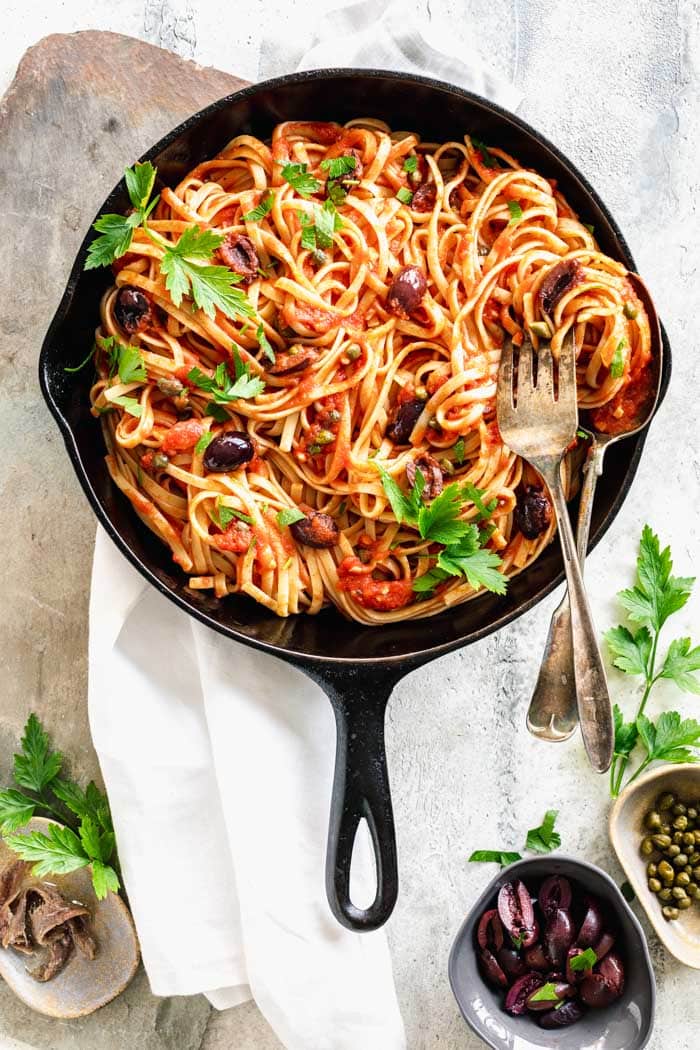 a black skillet with pasta puttanesca in it