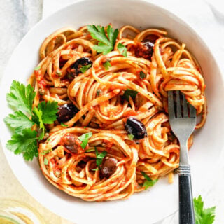 a closeup of a serving of the pasta puttanesca in a white bowl