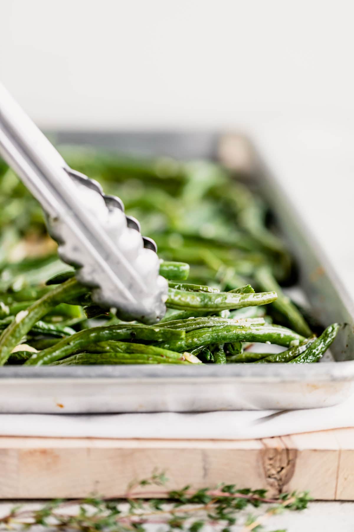 a pan of green beans from the side with a set of tongs grabbing a few