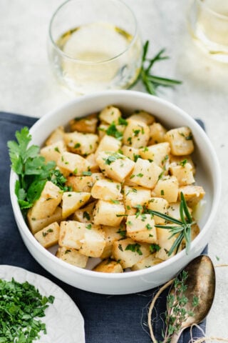 a modern white bowl filled with herbed celeriac with navy napkin with herbs