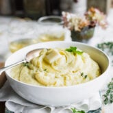 Mashed root veggie puree in a white bowl on a table with hydrangeas in a vase