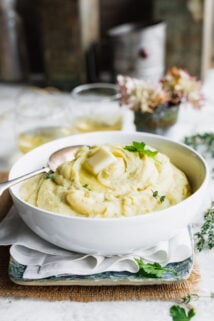 Mashed root veggie puree in a white bowl on a table with hydrangeas in a vase