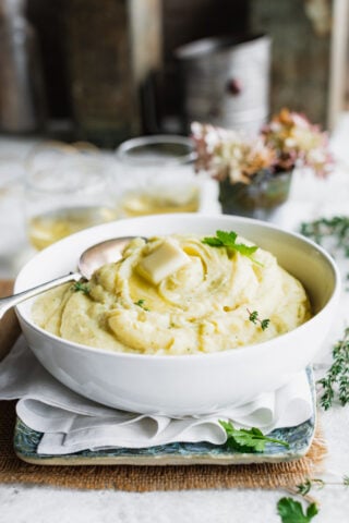 Mashed root veggie puree in a white bowl on a table with hydrangeas in a vase