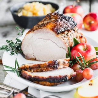pork loin sliced and on a platter with apples and herbs