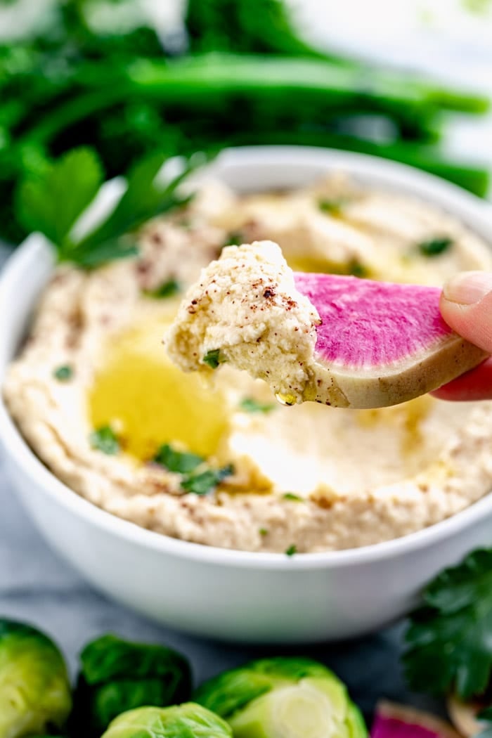 A slice of watermelon radish with a scoop of hummus on it
