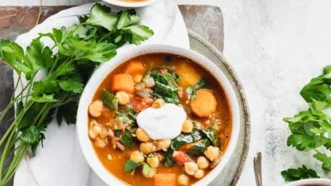 three bowls of stew on a table with bunches of herbs