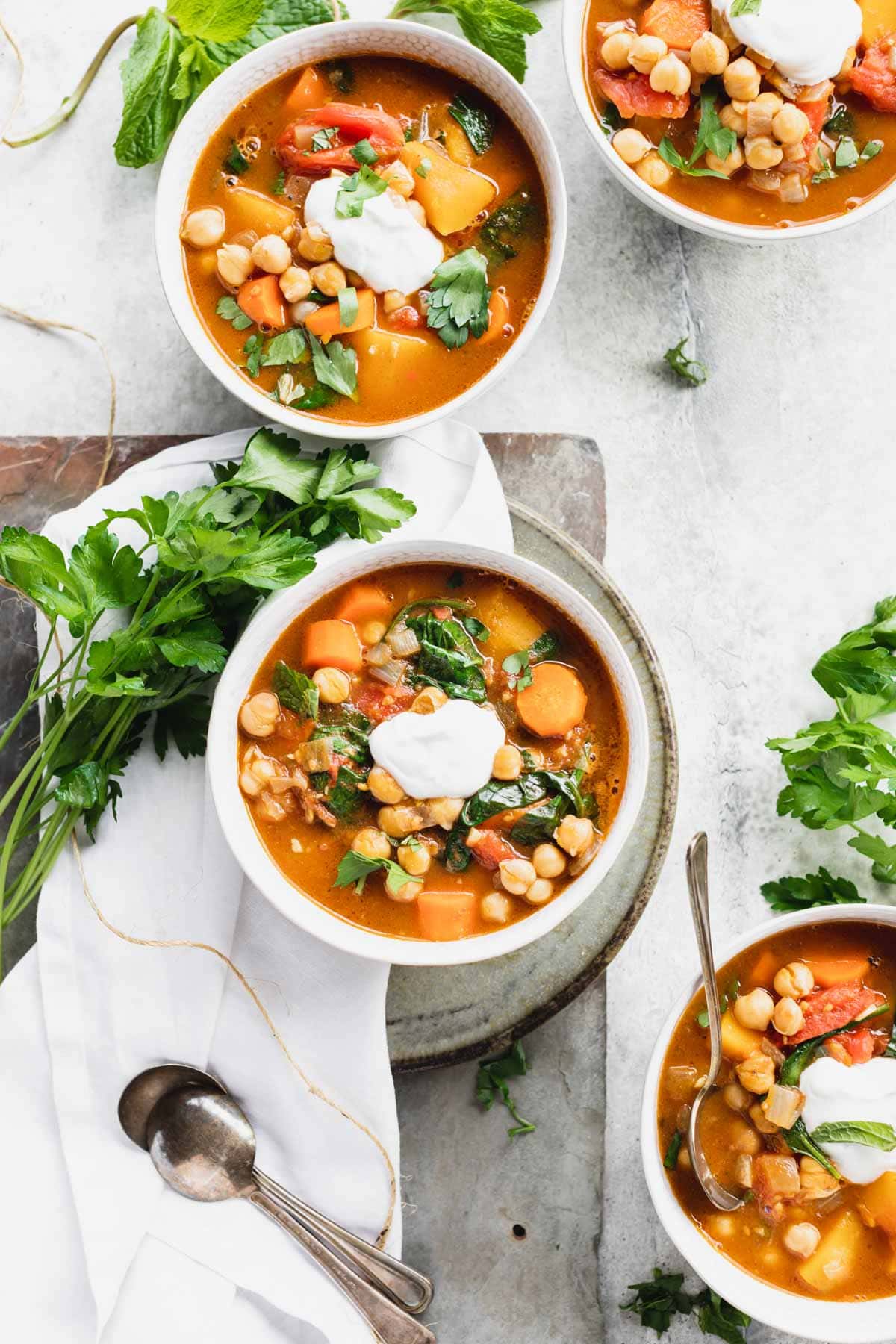 several bowls of stew on a white table with herbs