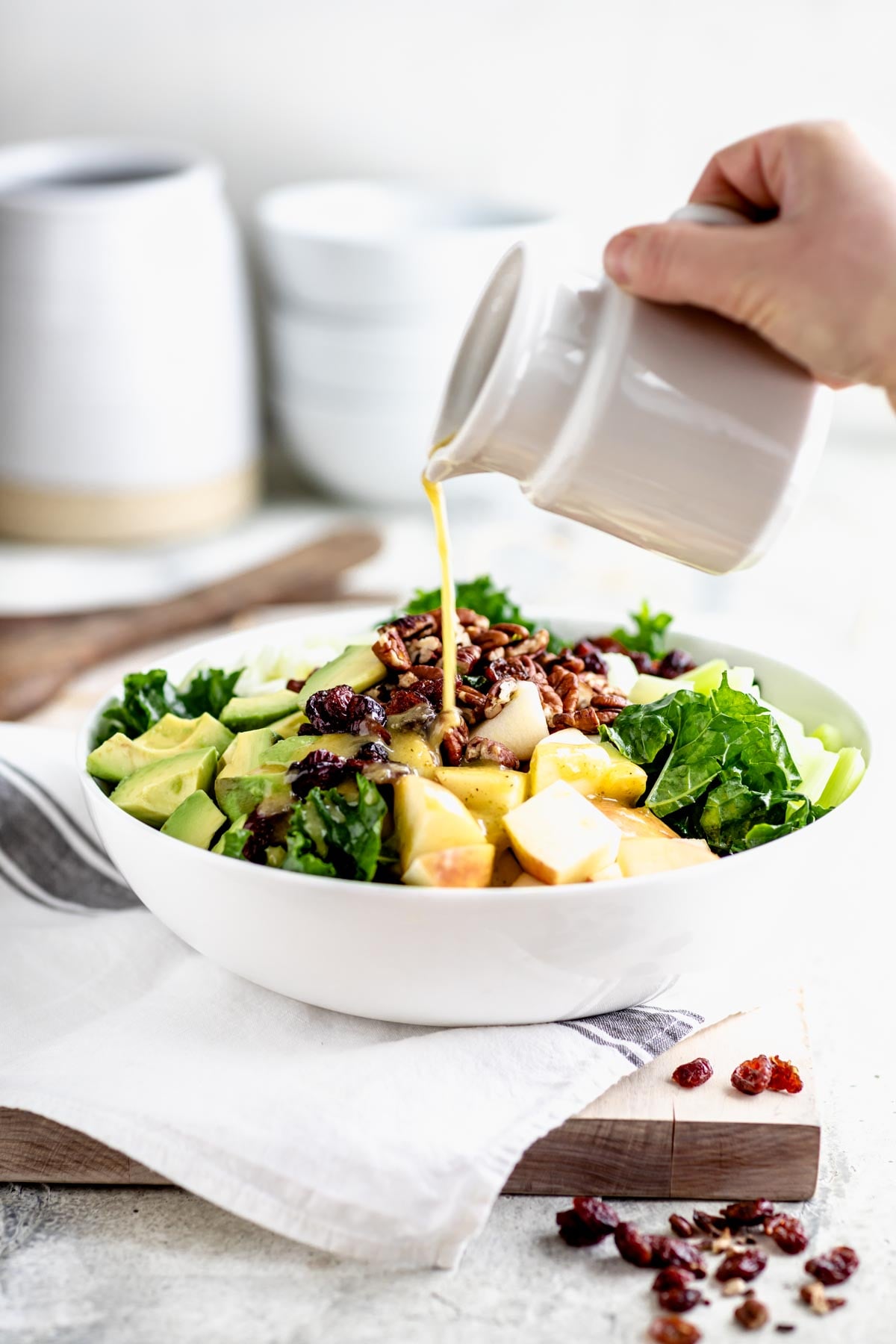 a white bowl with kale salad, a pitcher of dressing is being poured over it
