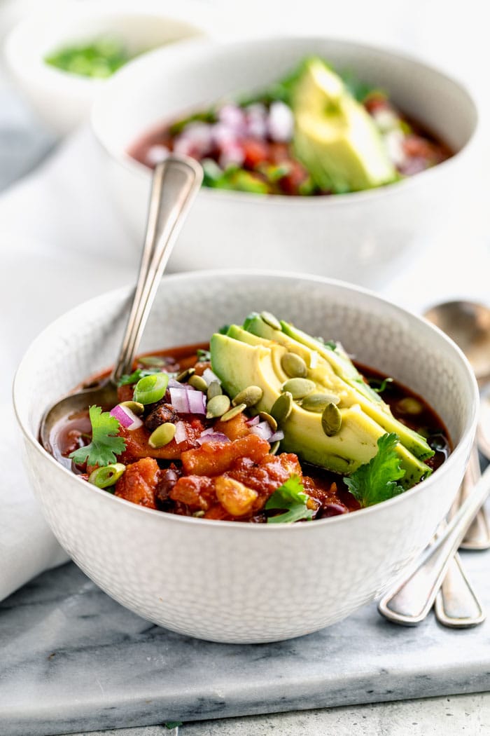 white bowls of chili from the side with avocado on top