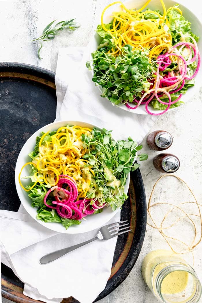 two bowls of colorful salad with a jar of dressing