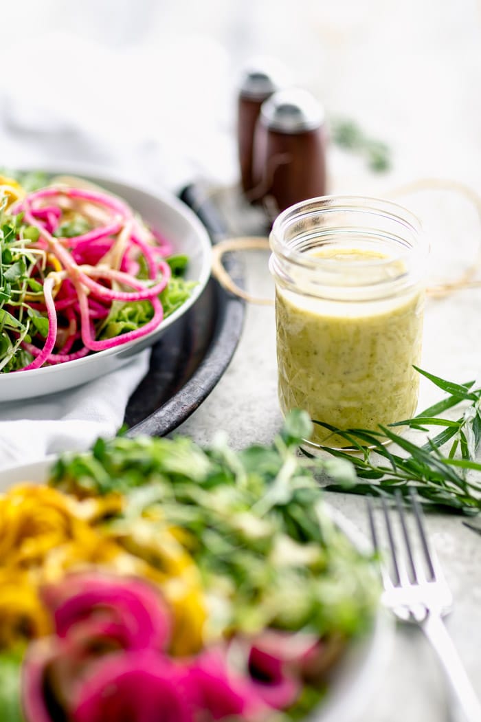 a jar of tarragon vinaigrette dressing on a table with salads