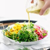 pouring dressing over microgreens and spiralized veggies