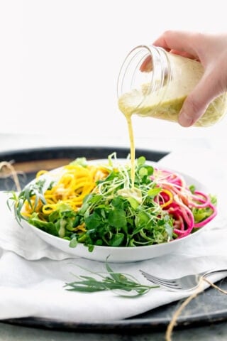 pouring dressing over microgreens and spiralized veggies