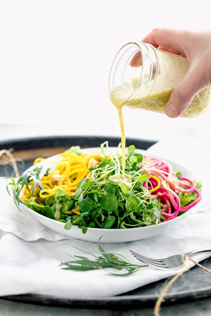 pouring dressing over microgreens and spiralized veggies