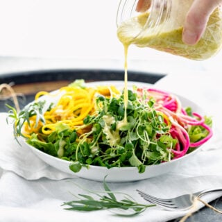 pouring tarragon dressing over a salad with colorful veggies