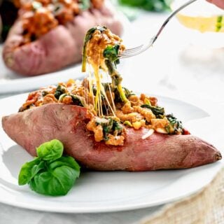side view of stuffed sweet potato. A forkful of the filling is begin lifted up and there is a lot of melted cheese