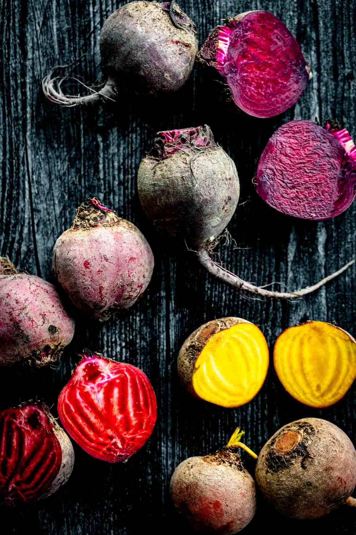 purple, golden and red and white striped beets cut open on a dark wooden table